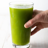 Hand holding a glass of green juice on a white background.  Dubrow Keto/Fusion Primo Celery.  Organic Celery Powder
