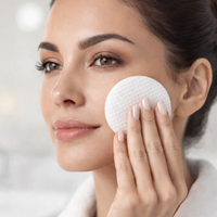 Woman using a white round makeup pad on her face against a neutral background