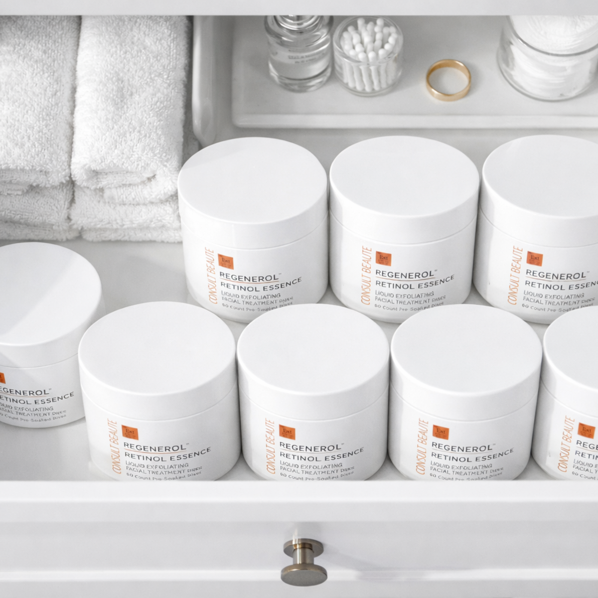 Multiple jars of Regenerol Retinol Essence on a bathroom shelf with towels and other items.